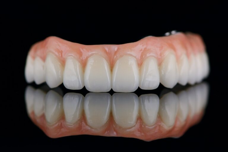 Image of a dentist holding a variety of "fake teeth" options, including a titanium implant, porcelain crown, and acrylic denture. No text on the image.